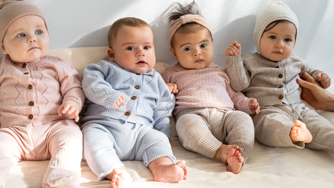 Four babies wearing minimalisma wool-cashmere knit outfits in sweet rose, clearwater and ecru melange. Inkaz cardigans and Itty pants. 